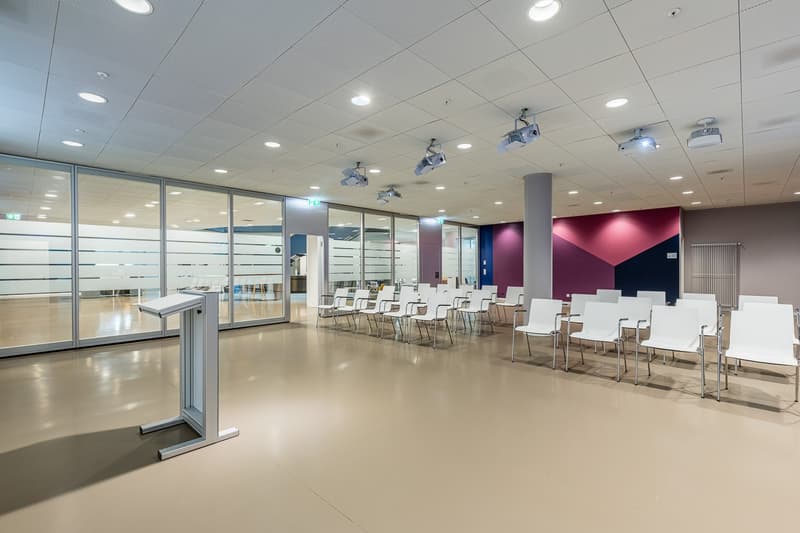 A conference room with multiple chairs, a podium, large glass walls, and projector lights