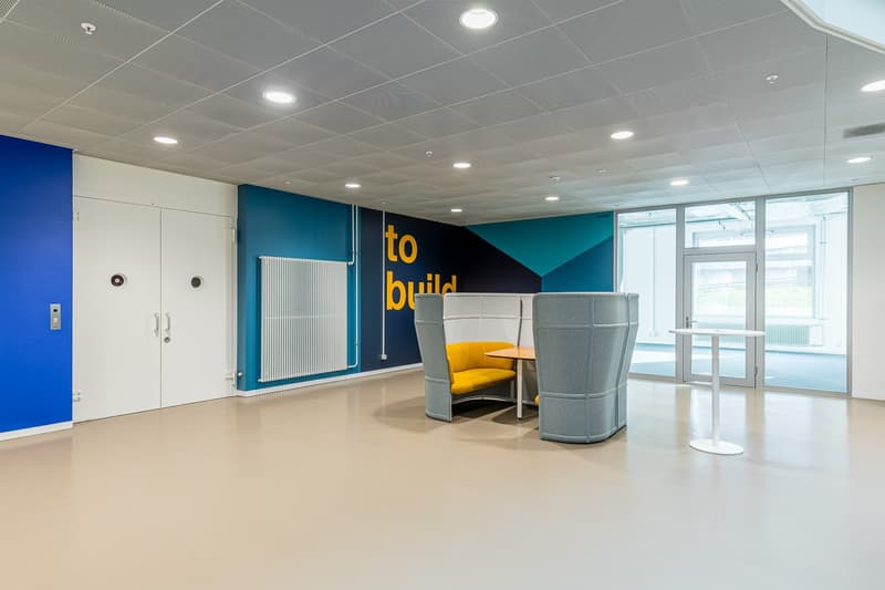Office space with blue and white walls, large entrance doors, yellow seating with a table, round table, glass doors to an exterior