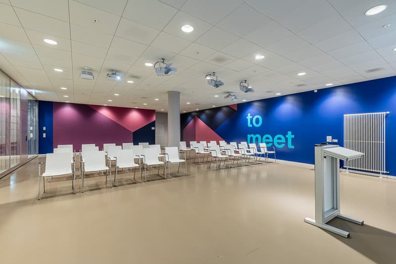 Conference room with white chairs, beige floor, blue and purple wall, white and red accents, text on wall, stage, podium