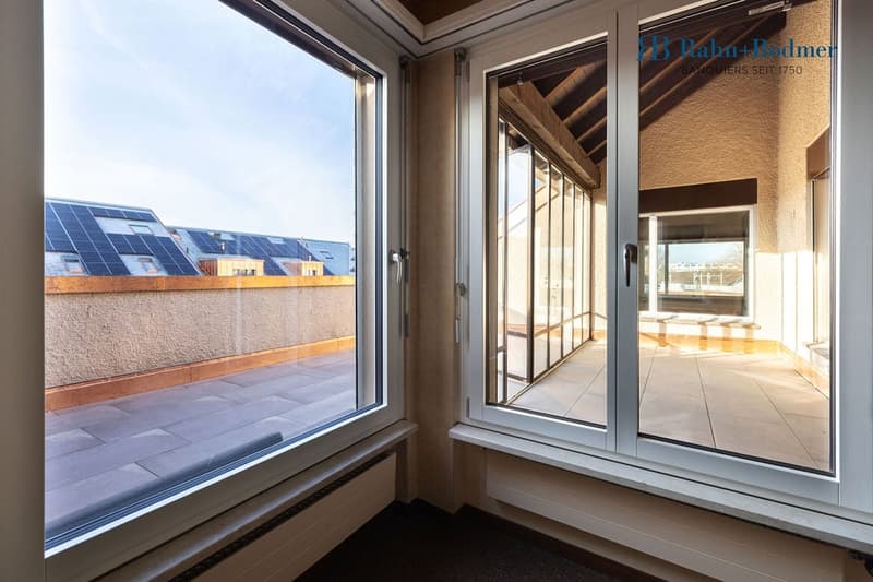 large windows, balcony, solar panels on other buildings, gray floor