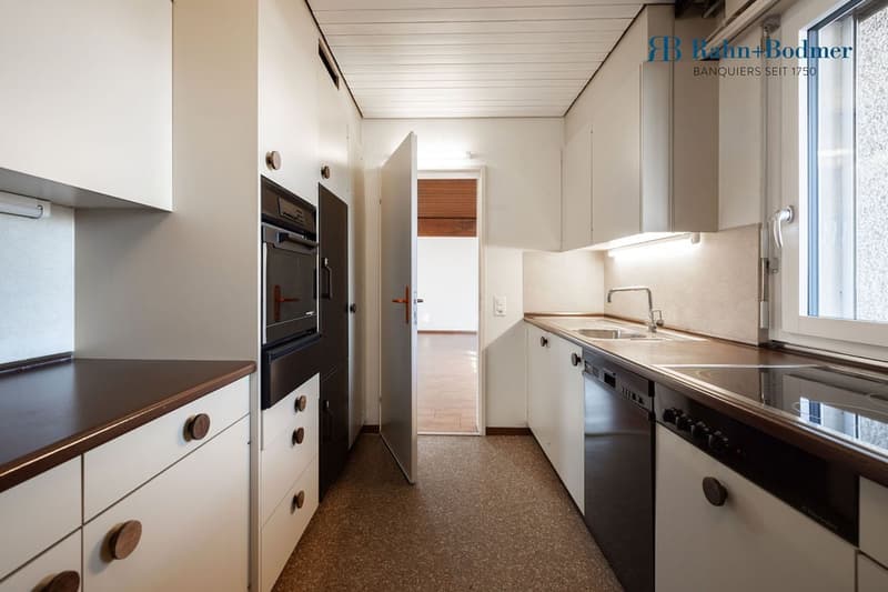 Modern kitchen with white cabinets, wooden countertops, integrated appliances including oven and dishwasher, and a sink with faucet.
