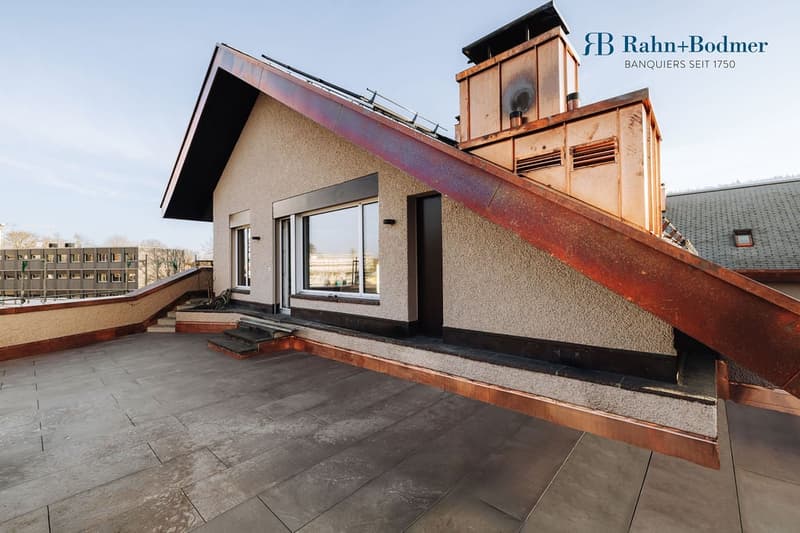 A house with a copper roof, featuring a tiled balcony/terrace with steps leading up to it, a chimney, and large windows.