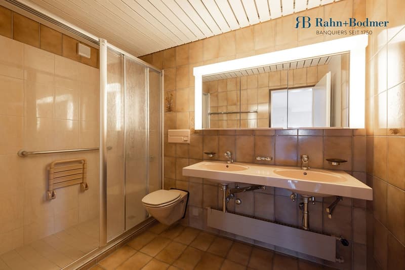 Double sink with mirror, shower, toilet, towel rack, and beige tiles