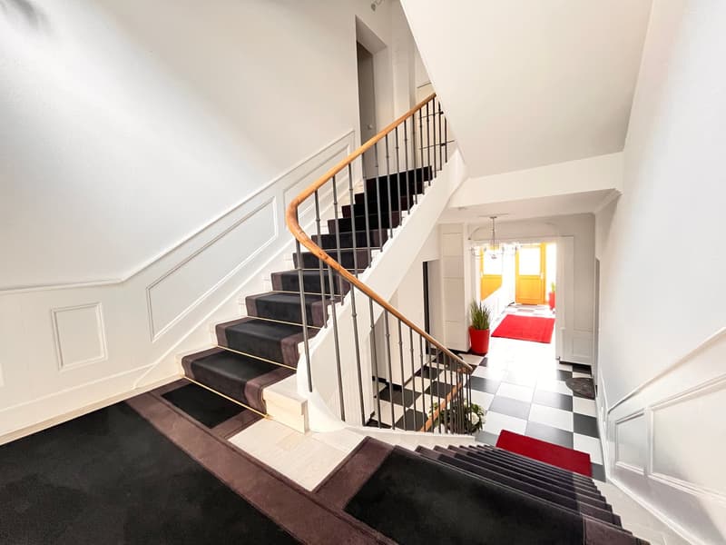 White house with wooden handrail staircase and tiled floor