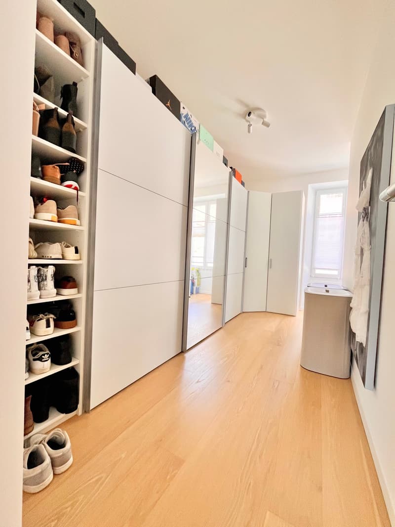 Spacious room with white built-in closets, shoe storage, mirrored closet door, hardwood floors, and a small white desk with drawers