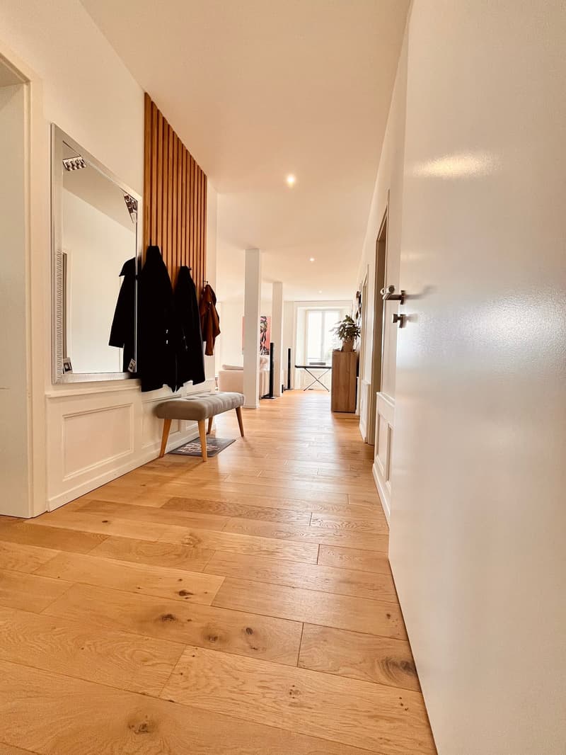 wooden floor, large mirror, clothes hanging on wall, bench, door, hallway