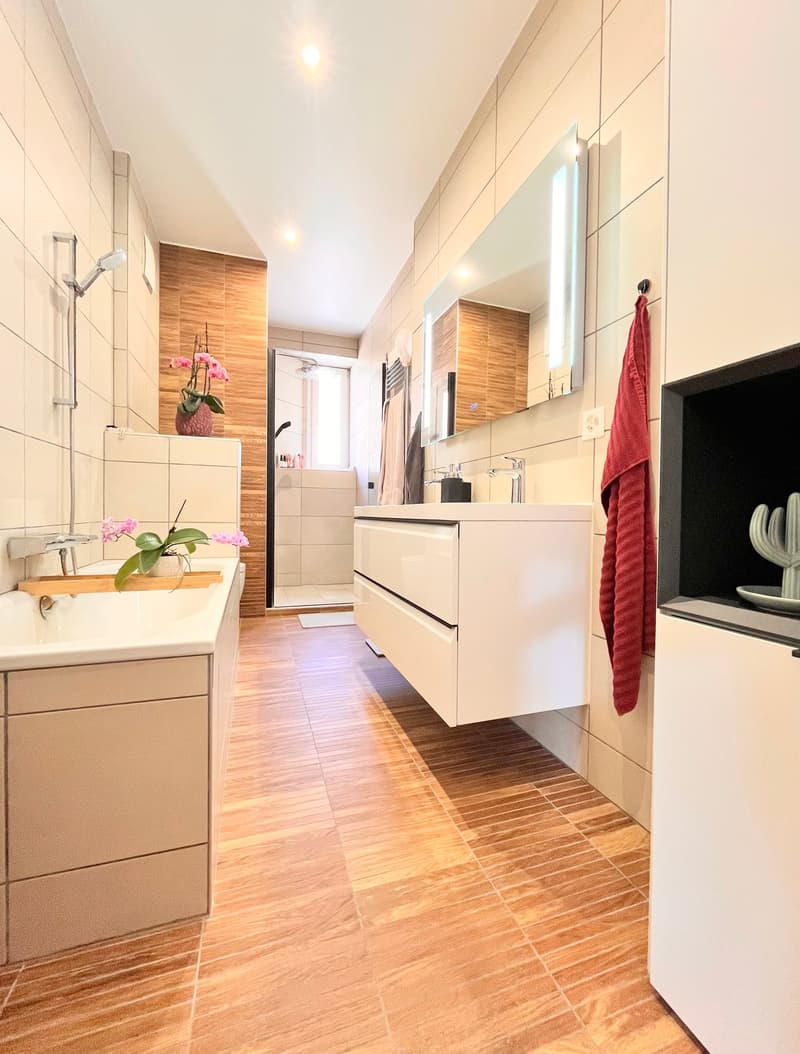 modern bathroom with wooden floor, white tiles, bathtub, shower, sink, mirror, wooden wall paneling, flower vase, towel rack