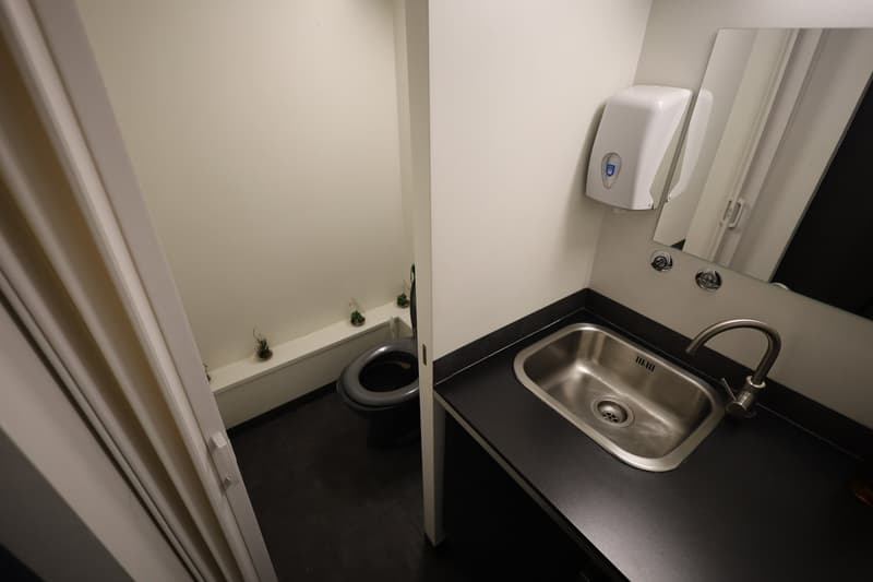 modern restroom with white walls, black tile floor, toilet, sink, mirror, soap dispenser