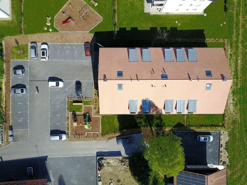 Row houses with parking area, red roofs, white windows, playground, solar panels, green lawns, car parked