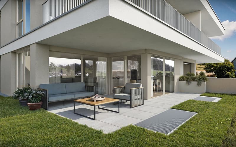 Modern house with balcony, large windows, outdoor seating area with couch and table, potted plants, paved patio, and green lawn
