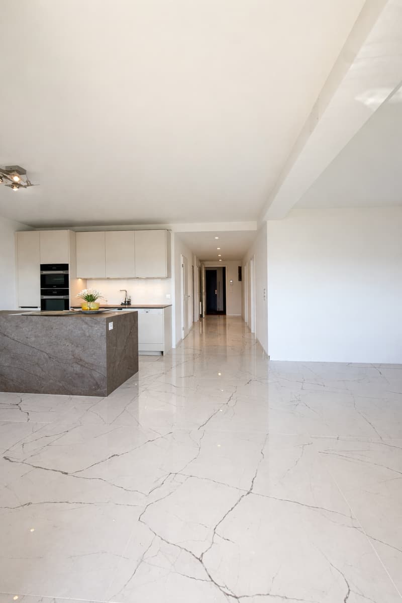 modern kitchen with marble countertop, white cabinets, white marble flooring, modern lighting, open hallway