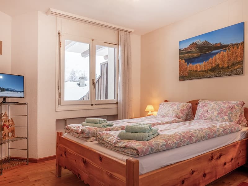 Bedroom with two beds, TV, artwork, lamp, towels, bedspreads, window with curtains