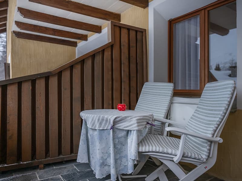 Balcony with a wooden railing, small table, two chairs, and a wooden window with curtains