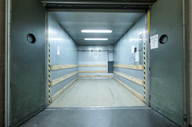 open double garage doors, empty room, wooden shelves, fluorescent ceiling lights, yellow caution stripes