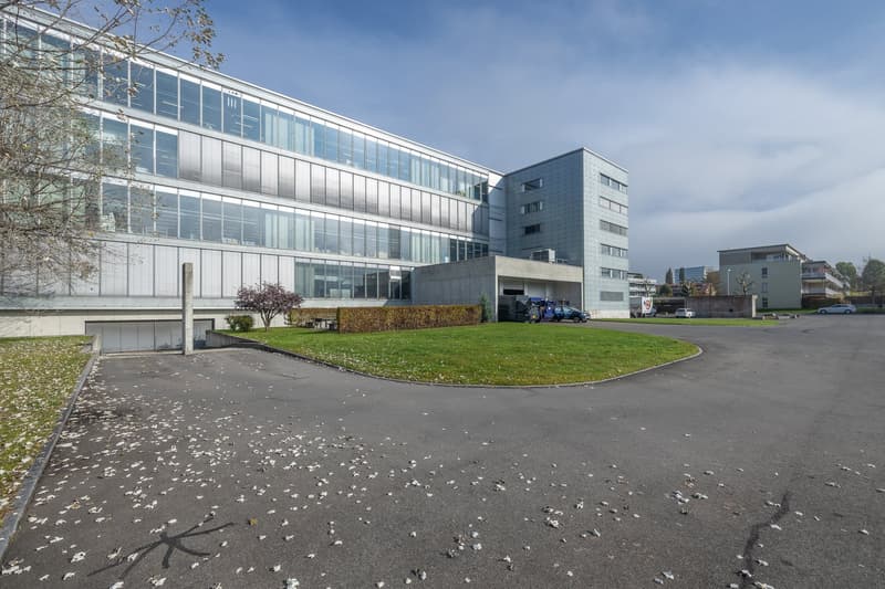 modern building with glass walls, metal panels, flat roof, garage on the side, large green lawn in front