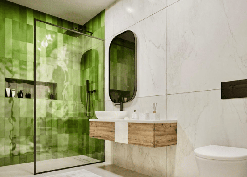 Bathroom with a green wall and glass shower, white marble walls, a wooden vanity, a white toilet, and a white sink with a mirror.