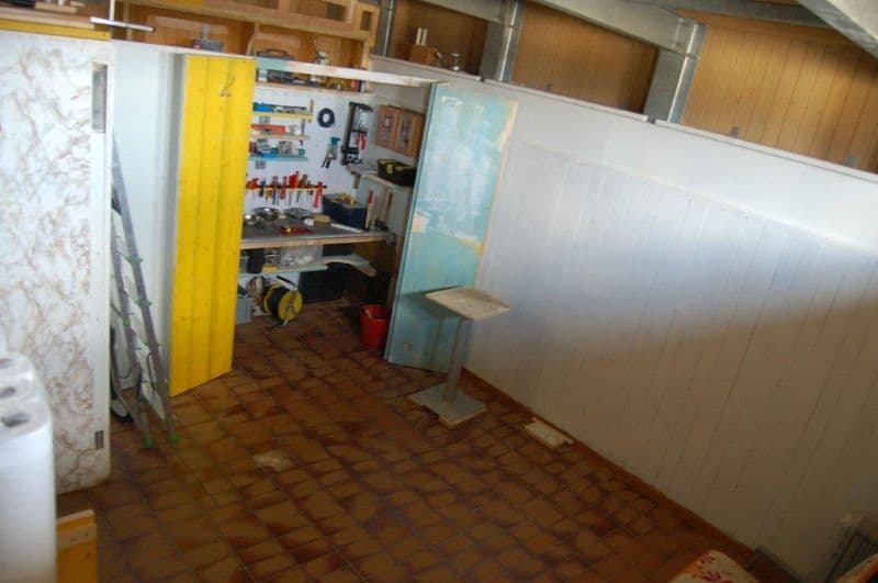 small room with tiled floor, wooden cabinets, tools and equipment on shelves, ladder, red bucket, table, stool