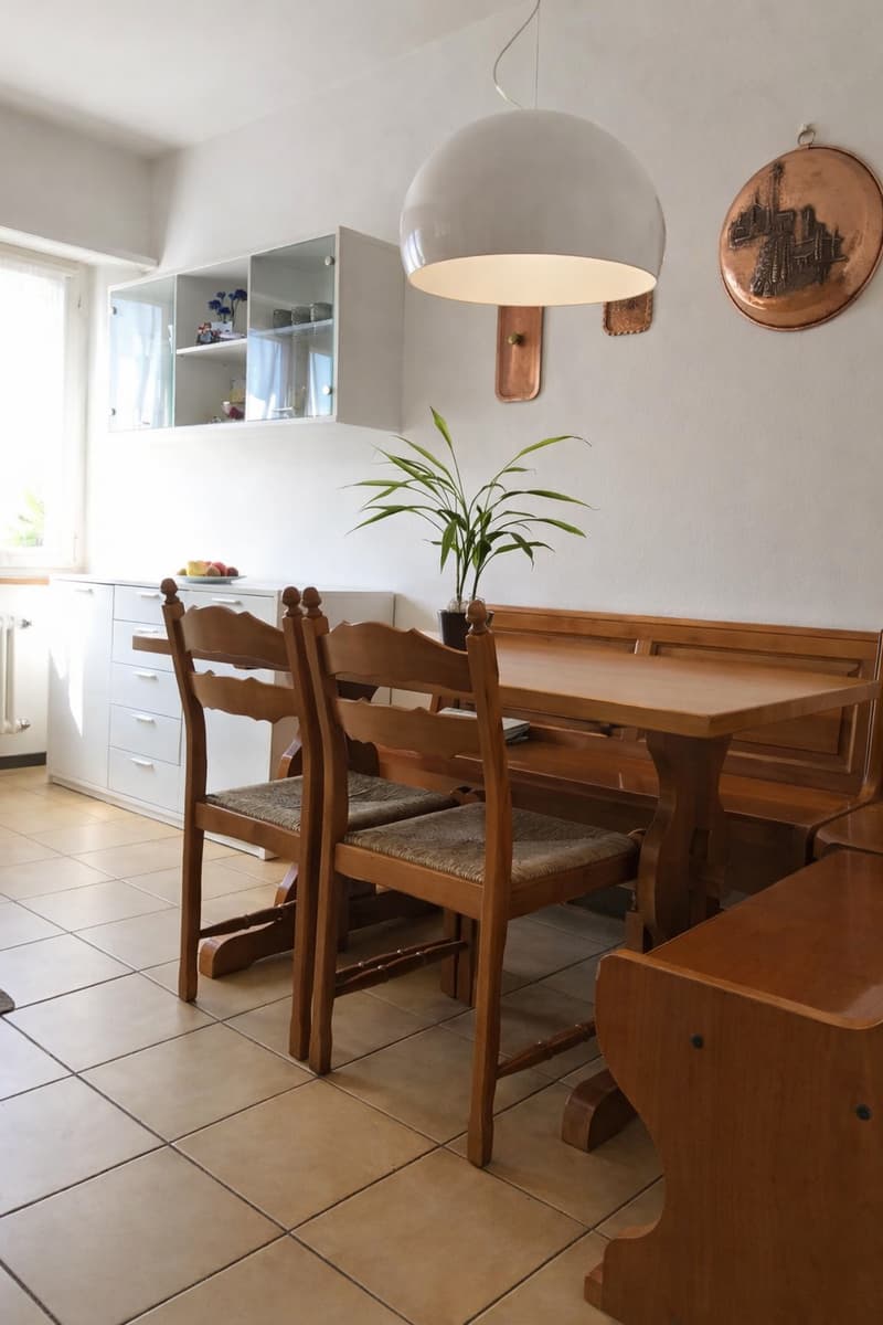 dining room, wooden table and chairs, potted plant, wooden bench, kitchen cabinets, large window, ceiling lamp