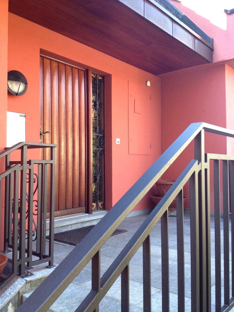 Exterior entrance with wooden door and metal railings, raised ground floor, orange walls, potted plants