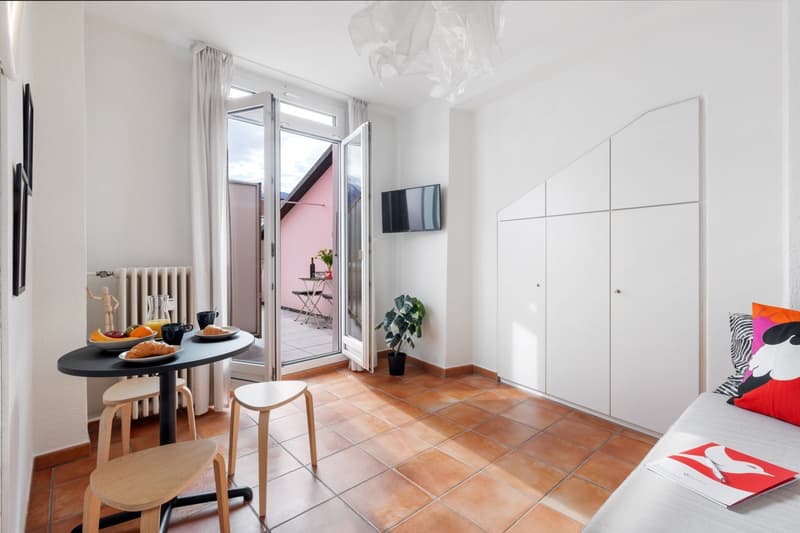 small dining area with table and chairs, sliding glass door to balcony, white walls, tiled floor, white cabinets, potted plant, TV