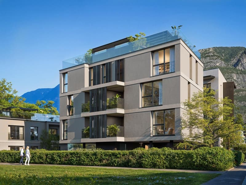 Modern multi-story building with glass balconies, surrounded by greenery and mountains in the background.