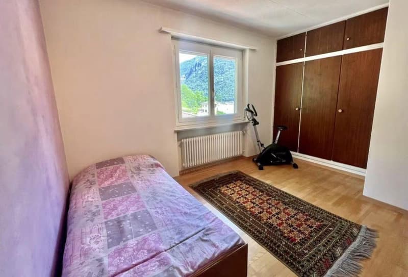 bedroom with bed, wooden floor, rug, exercise bike, wooden wardrobes, window with white frame, view of mountain and building