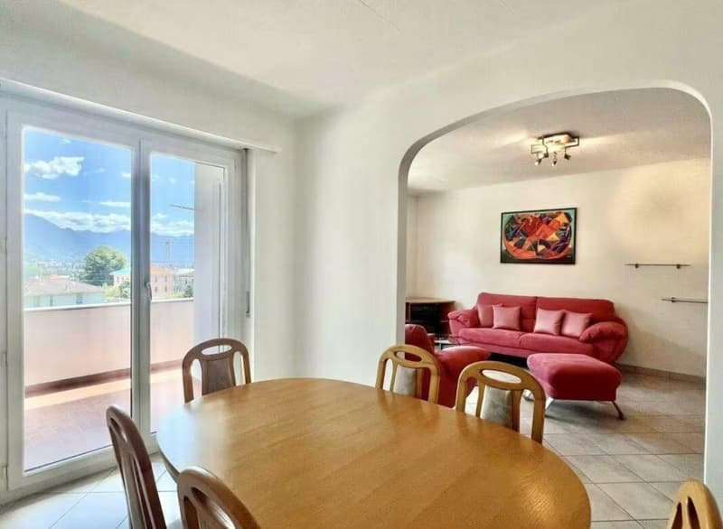 A balcony and a balcony door that opens to the outside, a dining table with chairs, a red couch, a picture frame on the wall