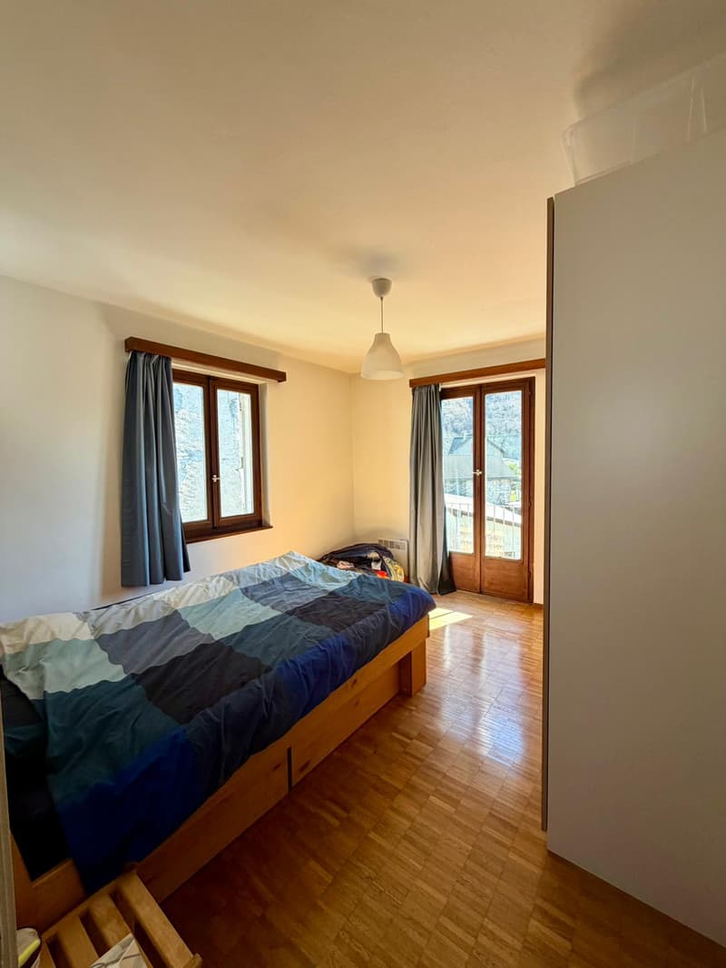 double bed with bedding, wooden floor, lamp, wooden window frame, balcony access, curtain, view of outside