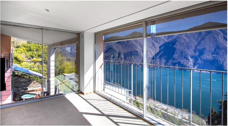 Spacious balcony with glass doors, metal railing, and a stunning view of the lake and mountains.