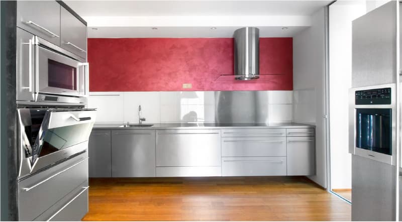 Modern kitchen with stainless steel appliances, red accent wall, wooden floor.