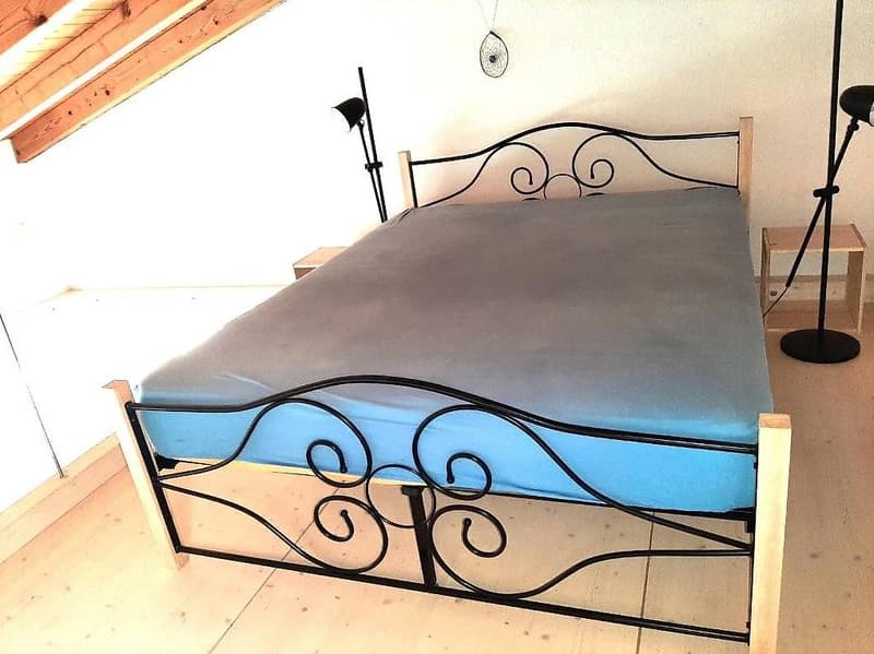 Black metal bed frame, blue mattress, wooden nightstands, black lamps, sloped ceiling
