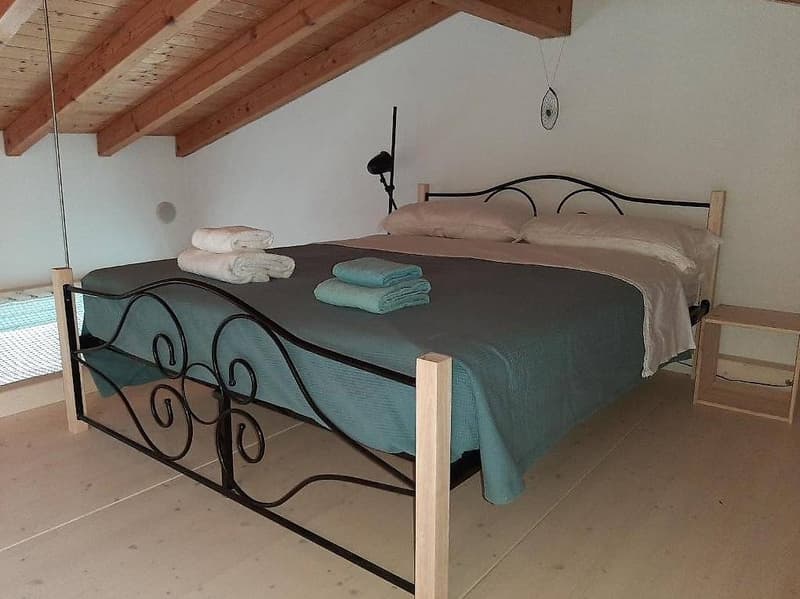 Bedroom with wooden ceiling, a double bed, pillows, blankets, and a nightstand.