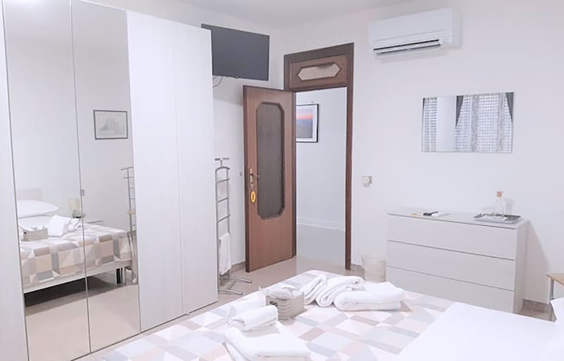 modern design, bed with white linen, two bedside tables, open wardrobe, white air conditioner, white nightstand with a small tray and a bottle on top