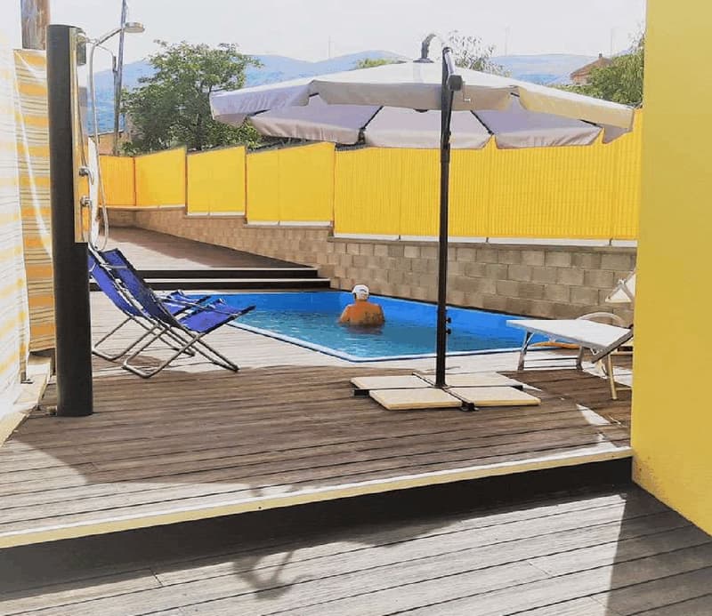 Outdoor swimming pool with chairs, umbrella, yellow fence, wooden deck