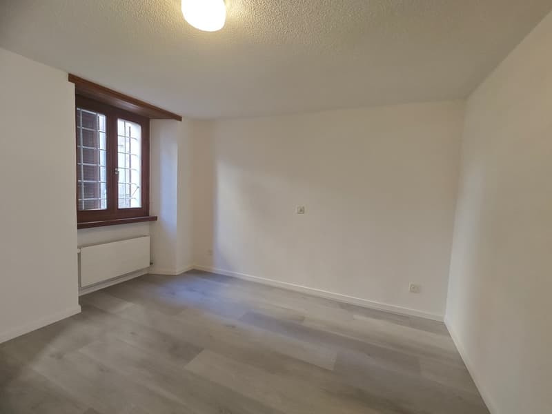Empty room with white walls, wooden window frame, radiator on the wall, windows, lights on the ceiling, wooden floor.