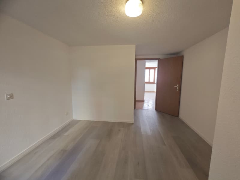 Empty room with white walls, wooden floor, open door, and a door leading to another room