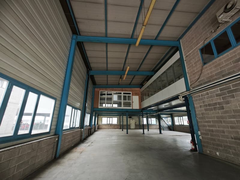 Empty warehouse with blue pillars, brick walls, large windows, and a concrete floor.