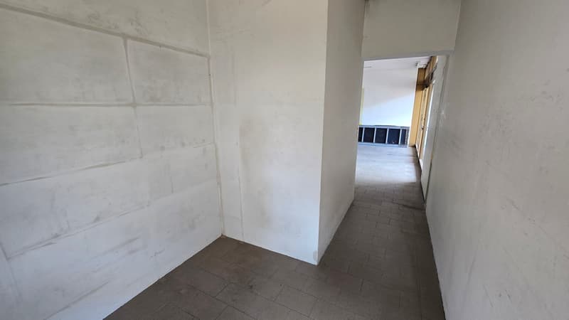 Empty corridor with white walls and tiled floor, leading to another room.