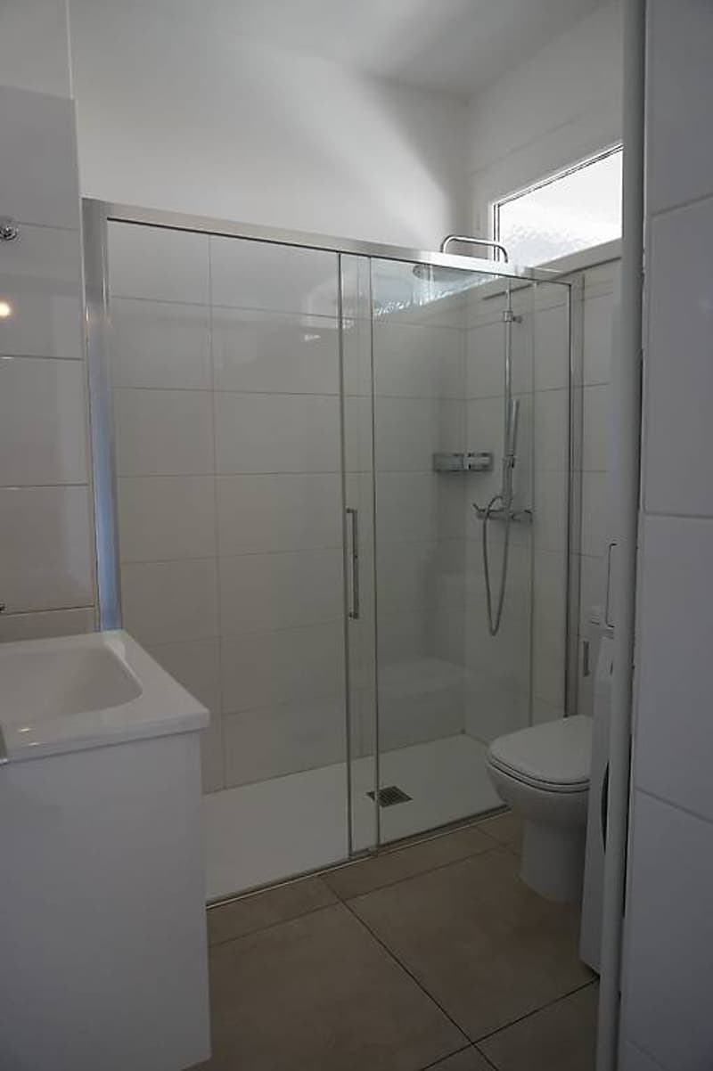 Glassed-in shower, tiled walls, white sink, white toilet, tiled floor