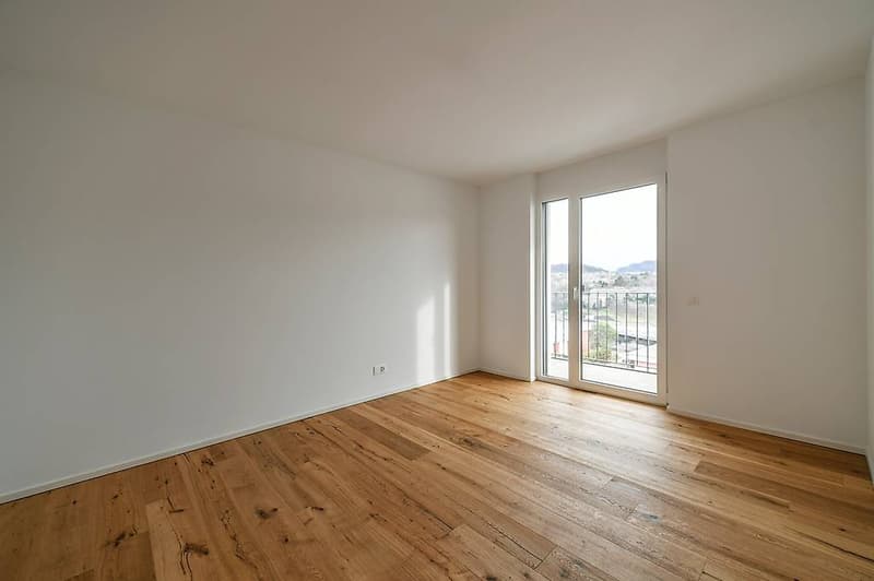 empty room, white walls, wooden floor, sliding glass doors leading to balcony, power outlet on the wall