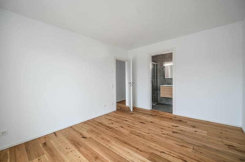 Empty room with white walls, wooden floors, an open door, and a shower