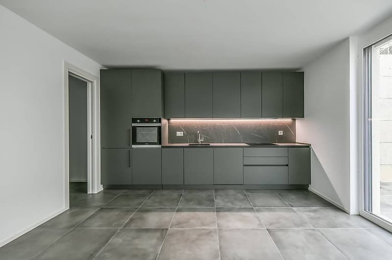 Modern kitchen with glass door, grey cabinetry, built-in oven, granite countertop, modern faucet, sink, tile flooring