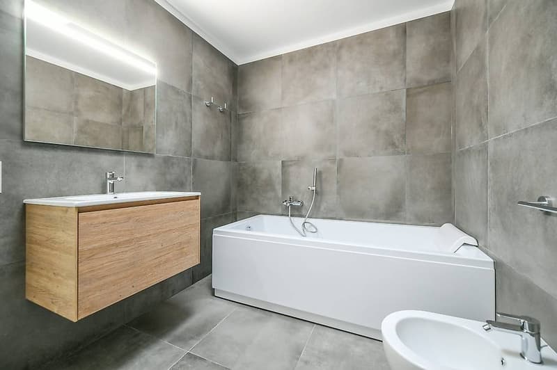 modern bathroom, gray tiled walls, wooden cabinet, white bathtub, modern vanity with a sink and mirror