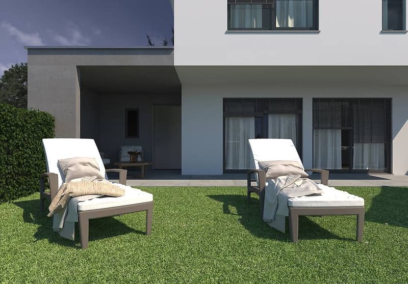 Two lounge chairs on a lush green grass lawn in front of a modern house