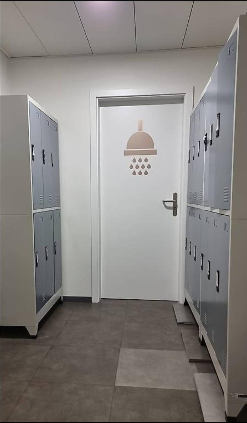 Empty locker room with grey lockers, white door, and tiled floor.