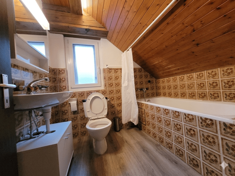 Bathroom with wooden ceiling, tiled walls, white sink, toilet, bathtub, and a window