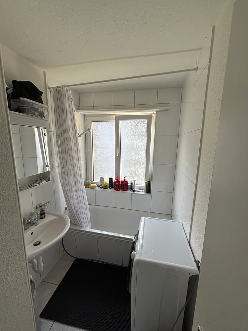 Bathroom with bathtub, sink, mirror, washing machine, window, and tiled walls