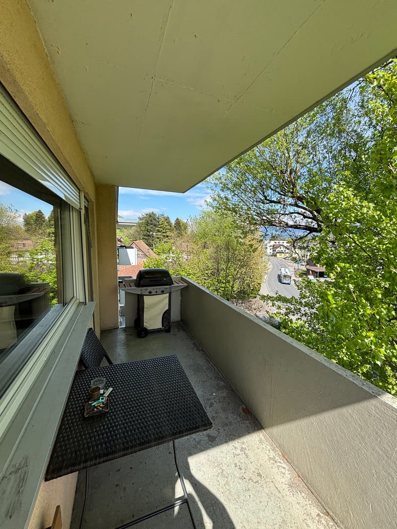 Balcony with table, grill, and view of the street and trees