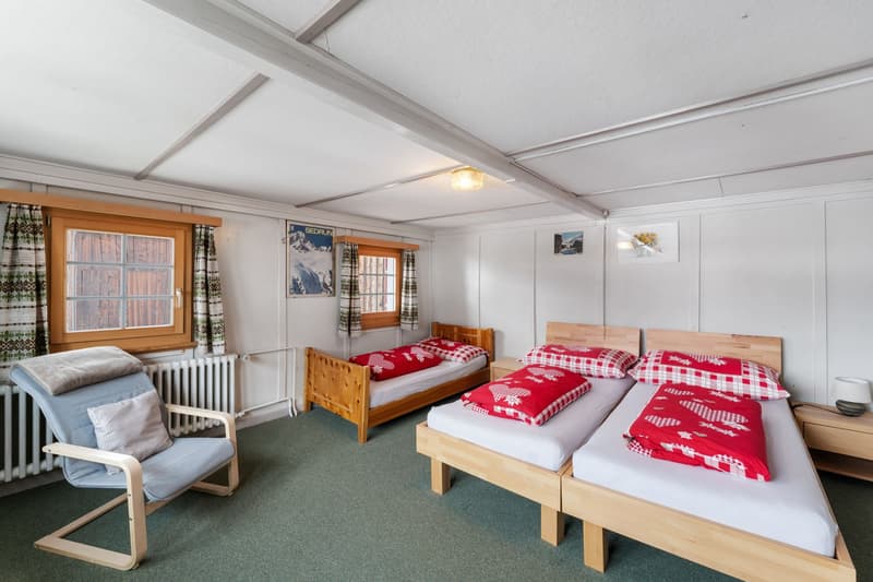Bedroom with three single beds, wooden chair, radiator, and two windows with curtains