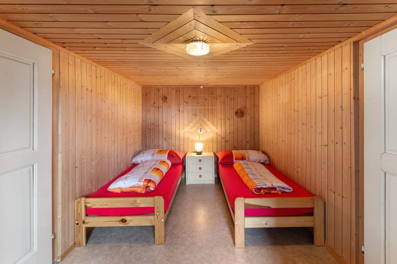 small room with two single beds, wooden walls, white nightstands, lamps